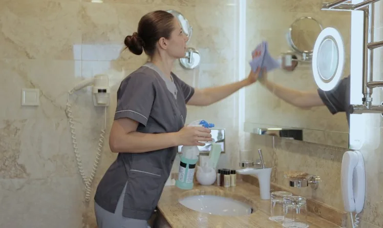 Camarera de pisos limpiando el espejo del baño de una habitación de hotel