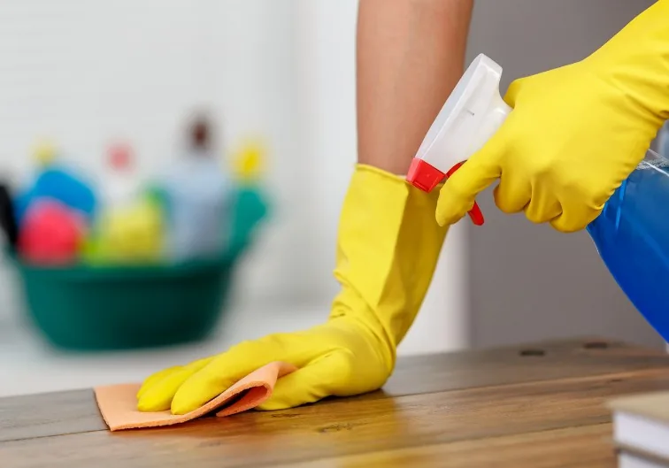 Limpieza de una mesa de madera con pulverizador y bayeta, con guantes de goma amarillos